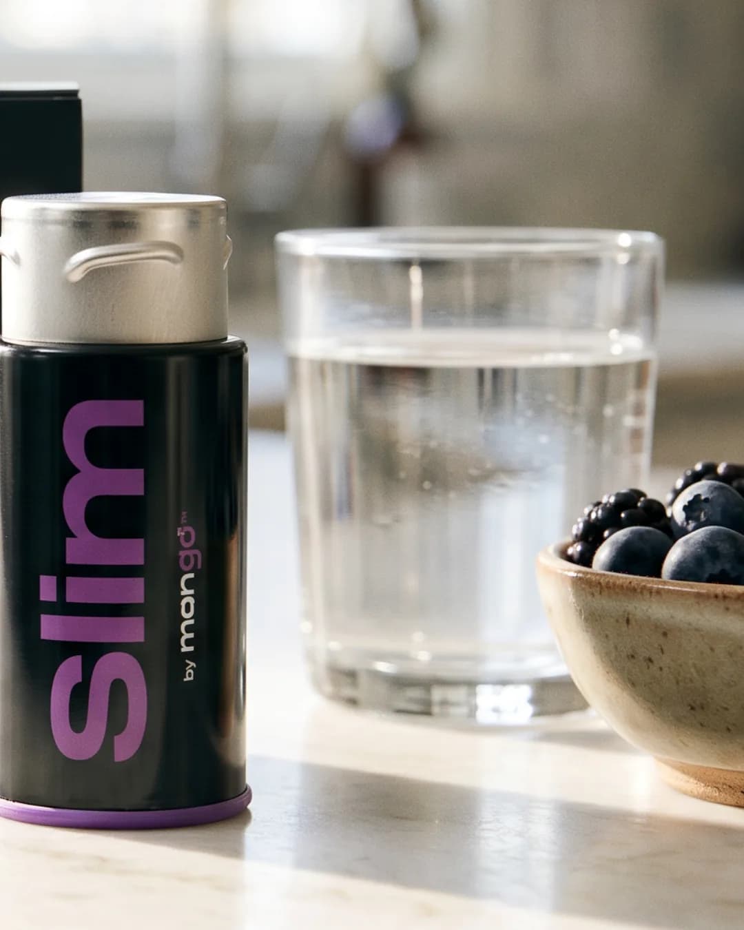 A black Slim tin on a kitchen counter beside a glass of water